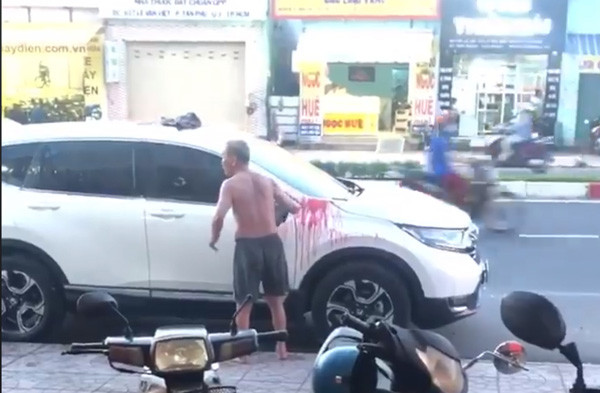 Người đàn ông lớn tuổi đang đổ sơn đỏ lên chiếc xe ôtô màu trắng (ảnh căt từ video clip).